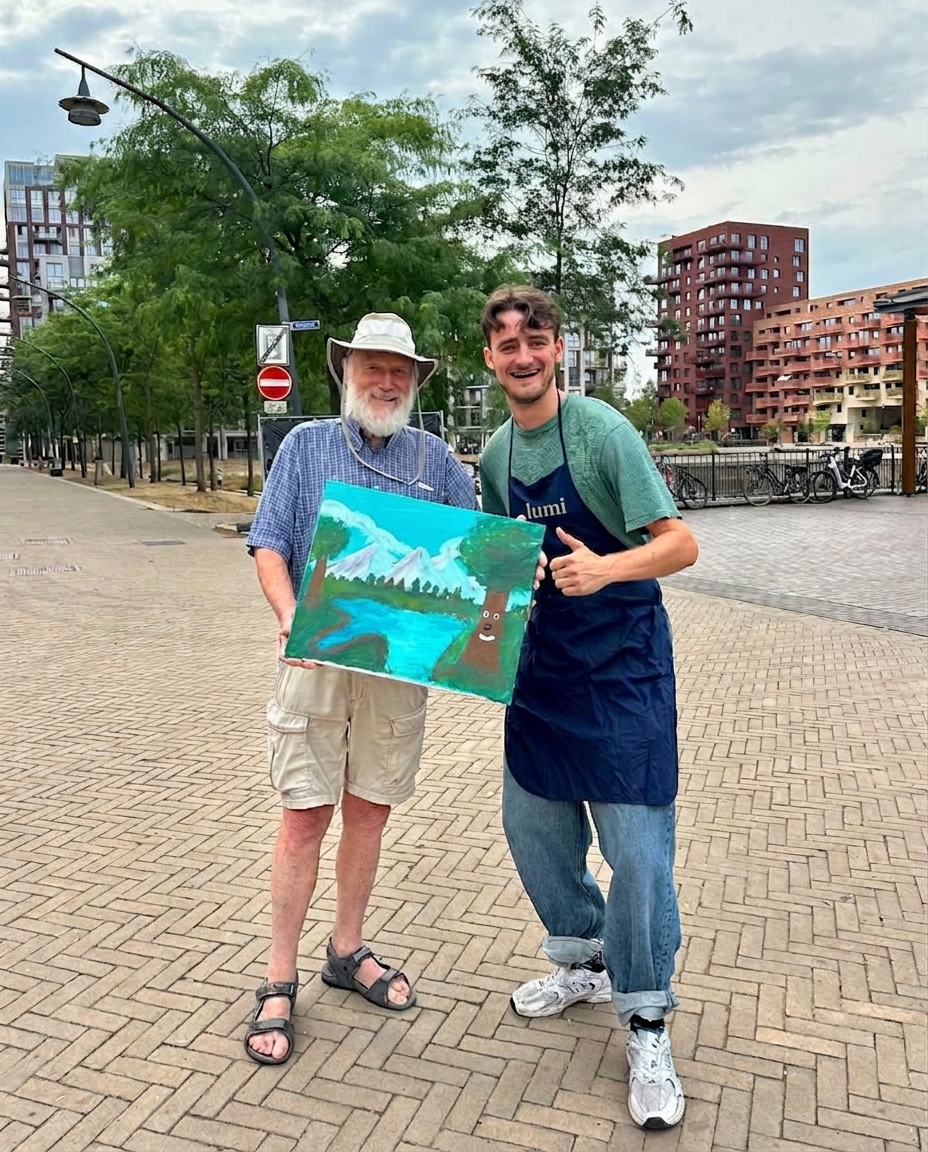 Deelnemer en workshopdocent met een geschilderd Bob Ross-landschap buiten op locatie